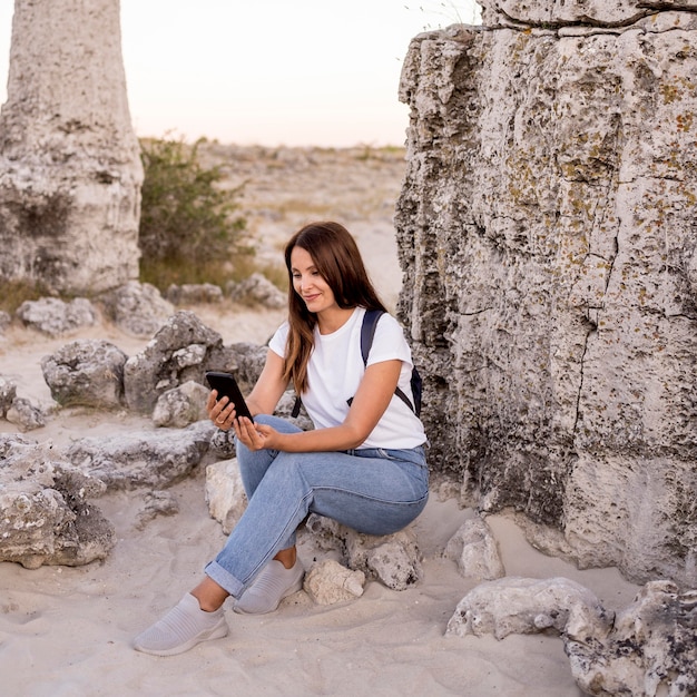 Donna di vista frontale che osserva sul suo telefono mentre era seduto su una roccia