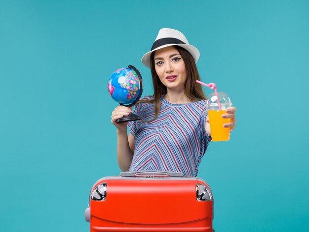 Donna di vista frontale in vacanza che tiene il succo e il globo sul viaggio di viaggio estivo di vacanza di viaggio del mare del fondo blu