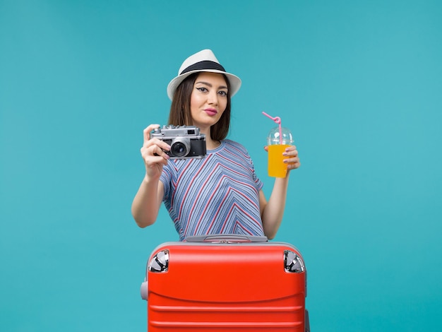 Donna di vista frontale in vacanza che tiene succo e macchina fotografica su uno sfondo blu viaggio estate viaggio viaggio vacanza mare
