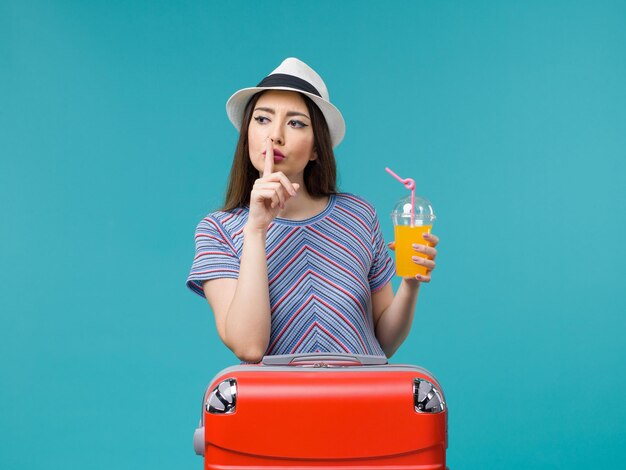 Donna di vista frontale in vacanza con la sua borsa rossa che tiene il suo succo su sfondo azzurro viaggio viaggio viaggio vacanza femminile