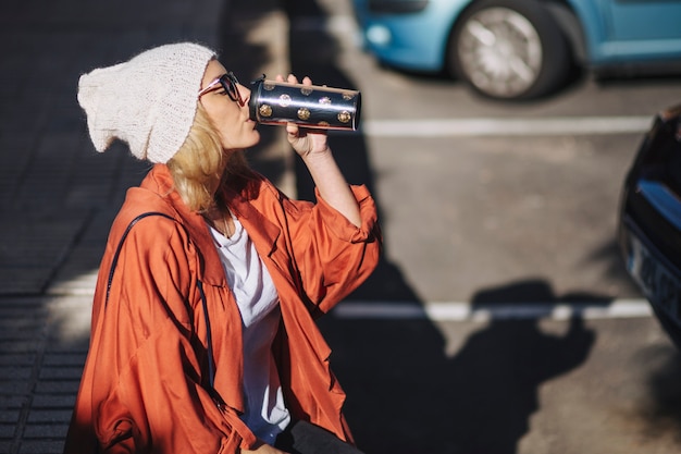 Donna di vista laterale che beve sul parcheggio