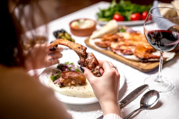 Donna di vista laterale che mangia la costola dell'agnello di kebab con un bicchiere di vino rosso