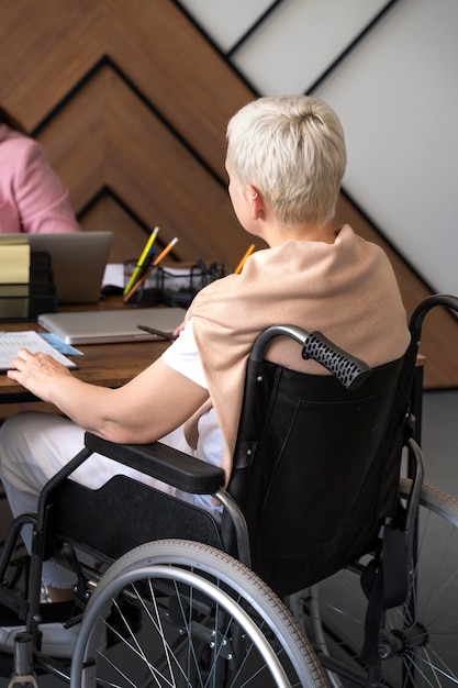 Donna di vista laterale in sedia a rotelle al lavoro