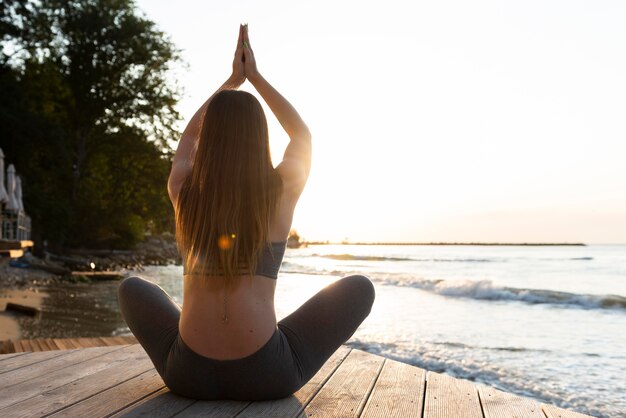 Donna di vista posteriore che fa yoga sulla spiaggia