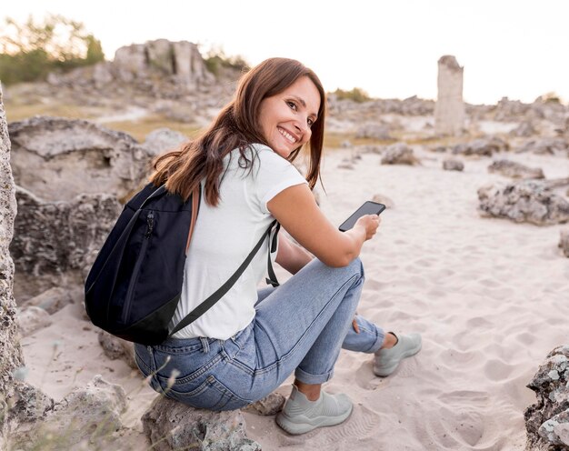 Donna di vista posteriore che sorride e che si siede su una roccia