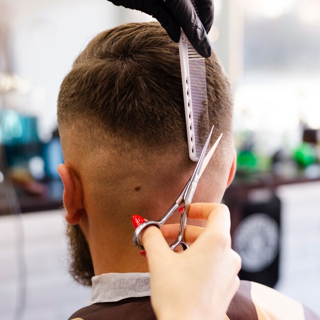 Donna di vista posteriore che taglia il primo piano dei capelli del suo cliente