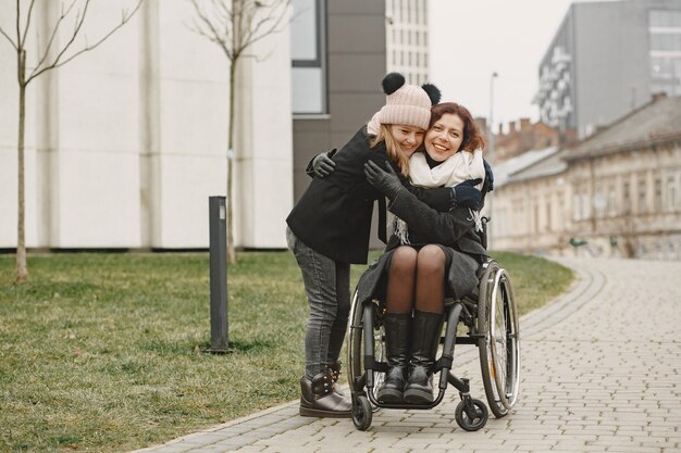 Donna disabile in sedia a rotelle con la figlia. Famiglia che cammina fuori al parco.