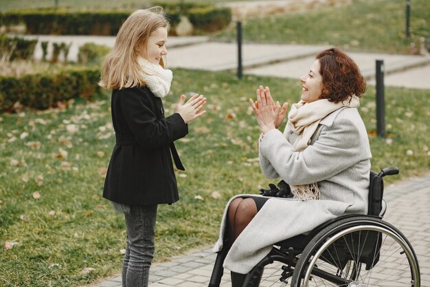 Donna disabile in sedia a rotelle con la figlia. Famiglia che cammina fuori al parco.