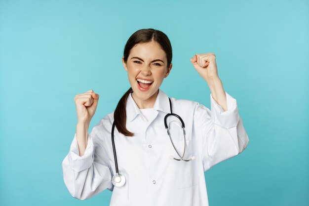 Donna dottore entusiasta che si rallegra di vincere e festeggiare raggiungere l'obiettivo in piedi in camice bianco ancora...