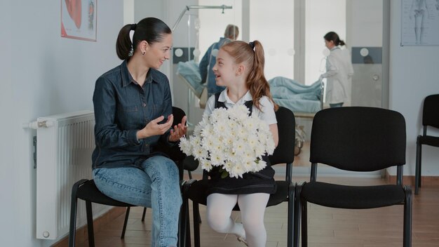 Donna e bambina che si preparano a visitare il paziente in sala d'attesa, con fiori per la persona malata. Madre e bambino in attesa di entrare nel reparto ospedaliero della struttura medica. Persone in sala d'attesa