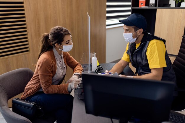 Donna e meccanico che indossano maschere facciali mentre parlano nell'ufficio dell'officina