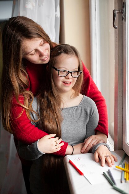 Donna e ragazza con sindrome di down che posa dalla finestra