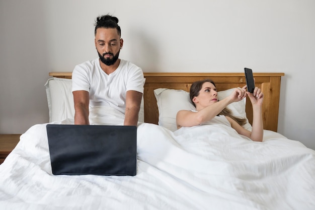 Donna e uomo che controllano i loro telefoni mentre sono a letto