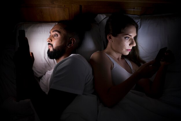 Donna e uomo che controllano i loro telefoni prima di dormire