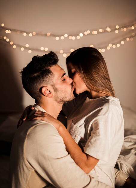 Donna e uomo che si baciano e si abbracciano sul letto nella stanza buia