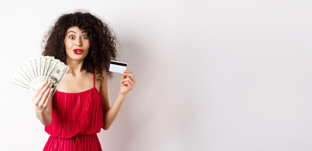 Donna eccitata che guarda con stupore e incredulità mostrando premi in dollari e carta di credito in plastica sta