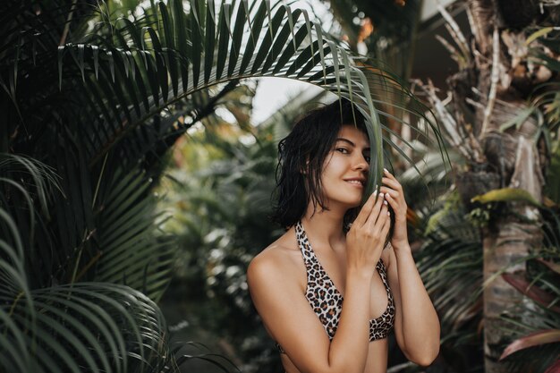 Donna eccitata con capelli scuri che propone al resort esotico. Bella giovane donna che si diverte durante le vacanze.