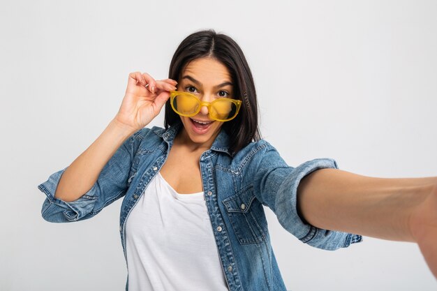 Donna eccitata sorridente attraente che fa la foto del selfie con la faccia sorpresa isolata su bianco