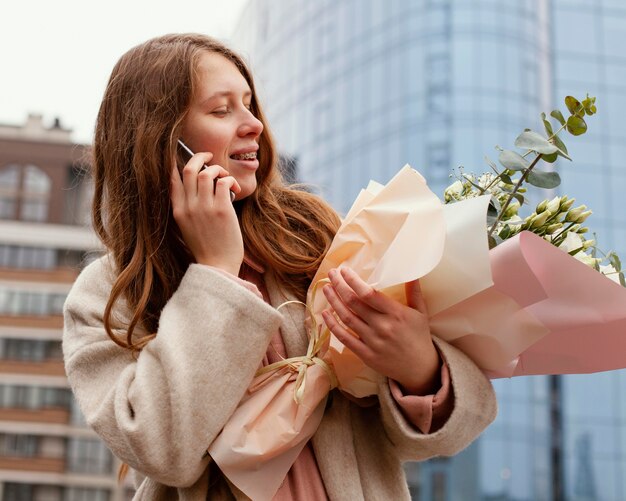 Donna elegante all'aperto conversando al telefono e tenendo il mazzo di fiori