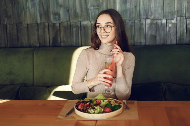 Donna elegante che si siede al tavolo con cocktail e insalata