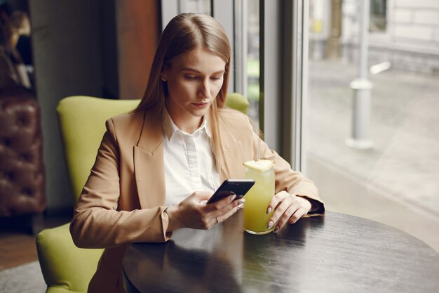 Donna elegante che si siede al tavolo con cocktail e telefono