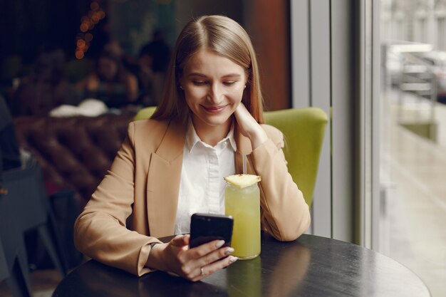 Donna elegante che si siede al tavolo con cocktail e telefono