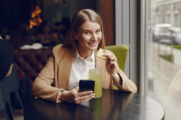 Donna elegante che si siede al tavolo con cocktail e telefono