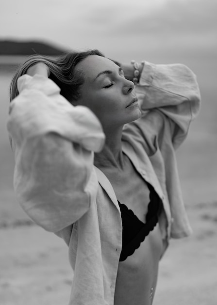 Donna elegante in abito casual in posa sulla spiaggia solitaria con tempo nuvoloso In bianco e nero