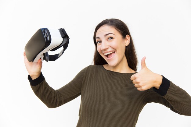 Donna emozionante allegra che tiene la cuffia avricolare di VR e che fa come