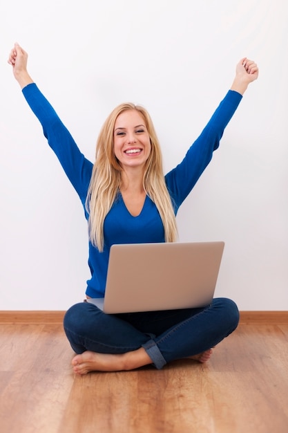 Donna emozionante con il computer portatile che si siede sul pavimento