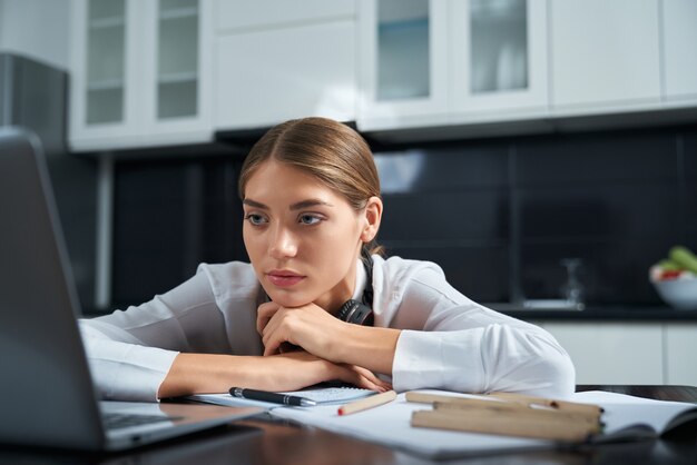 Donna esaurita che si siede al tavolo e lavora al computer portatile