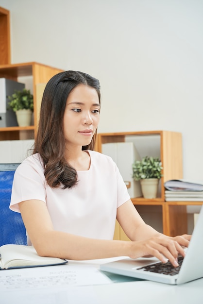 Donna etnica moderna che lavora con il computer portatile in ufficio