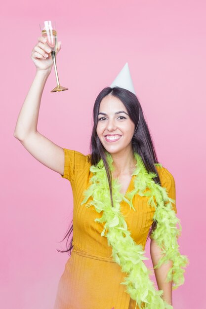 Donna felice che alza il pane tostato del champagne che porta boa e cappello del partito