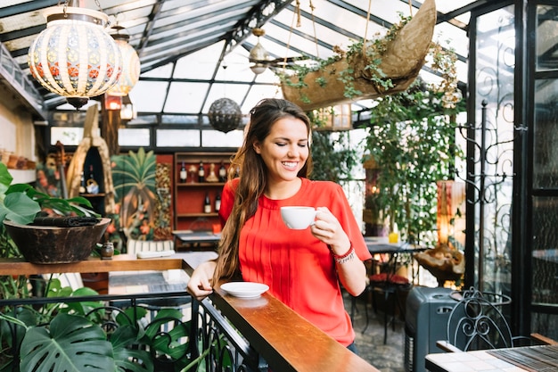 Donna felice che beve tazza di caffè nella caffetteria