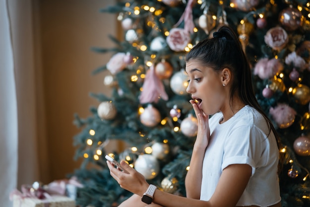 Donna felice che ha videochiamata con la famiglia o gli amici. La giovane donna utilizza una tavoletta digitale vicino all'albero festivo decorato a casa.