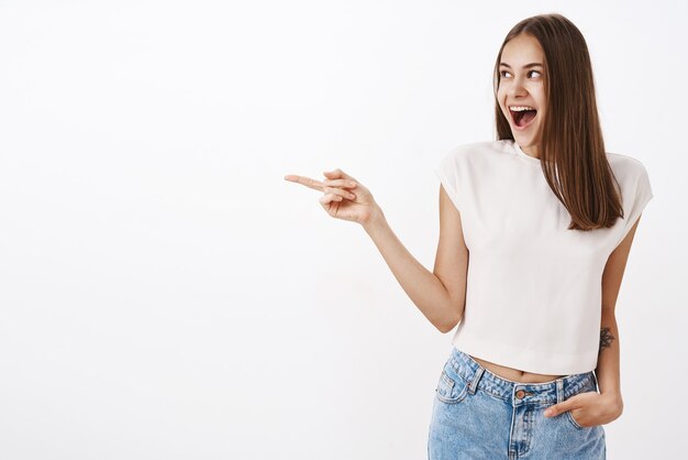 Donna felice che indica e che guarda a sinistra con un ampio sorriso soddisfatto e spensierato che tiene la mano in tasca dei jeans