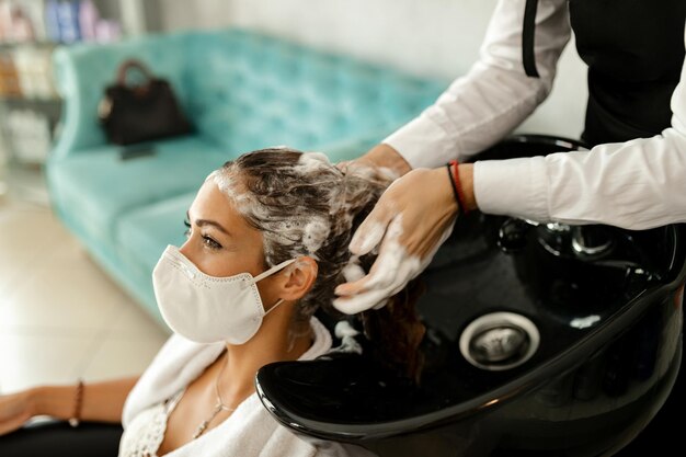 Donna felice che indossa una maschera protettiva durante il lavaggio dei capelli dal parrucchiere