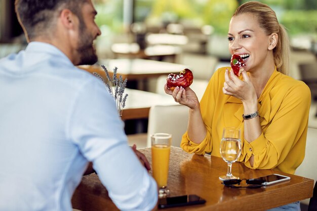 Donna felice che mangia ciambelle e parla con il suo ragazzo in un caffè