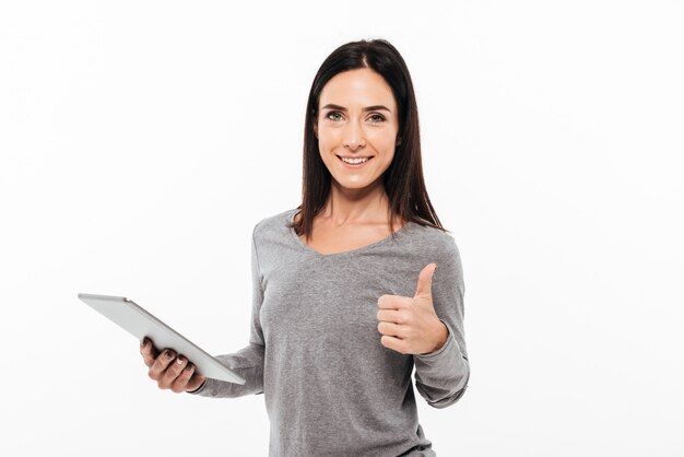 Donna felice che mostra i pollici su facendo uso del computer della compressa.