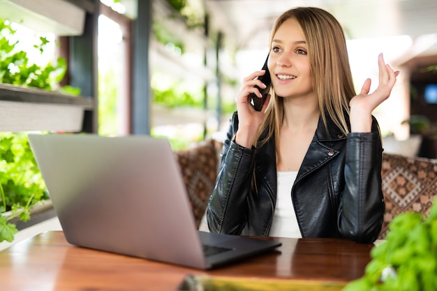 Donna felice che parla al telefono e usa il laptop in una caffetteria