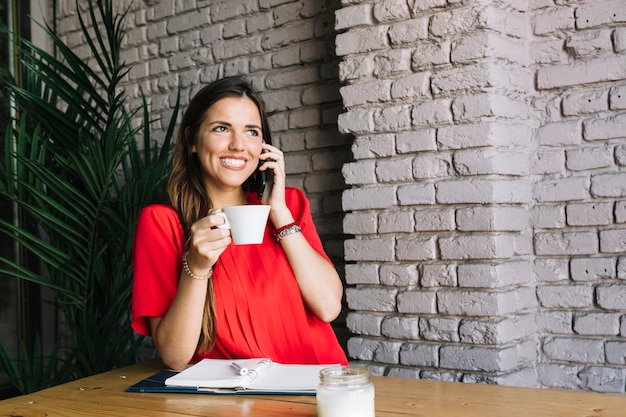 Donna felice che parla sul cellulare mentre bevendo caffè