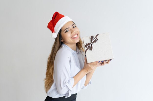 Donna felice che porta cappello di Babbo Natale e che tiene il contenitore di regalo