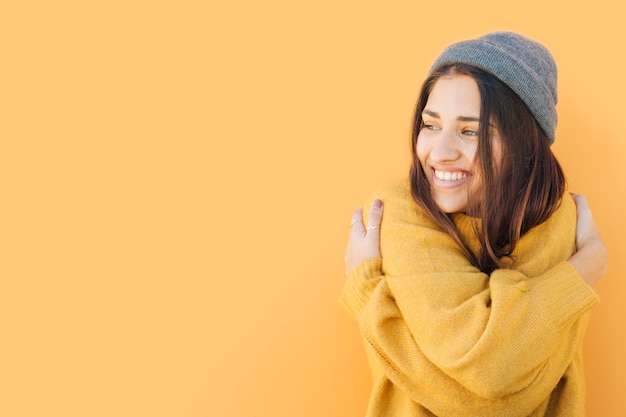 donna felice che porta cappello lavorato a maglia che si abbraccia su sfondo giallo