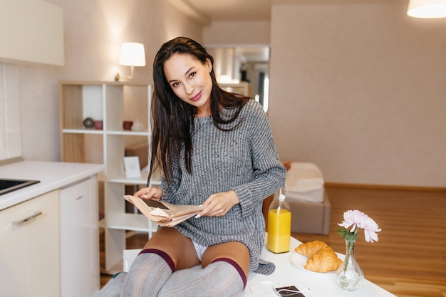 Donna felice che posa allegramente nella sua stanza con il giornale che gode del succo d'arancia