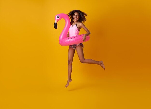 Donna felice che salta con anello di gomma fenicottero su sfondo giallo copyspace donna rilassante sulla spiaggia