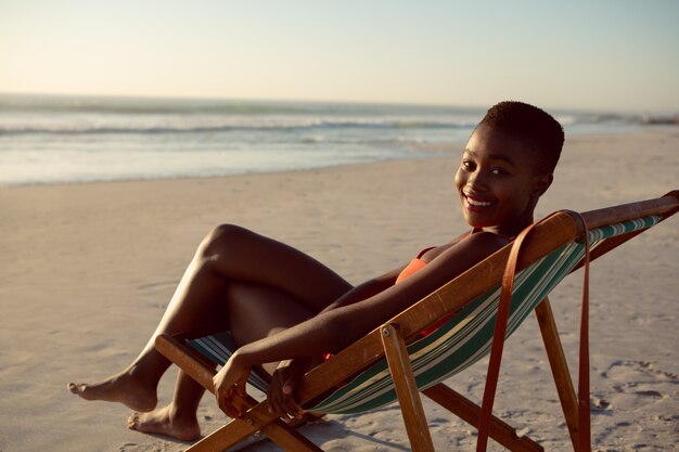 Donna felice che si rilassa in una sedia di spiaggia sulla spiaggia