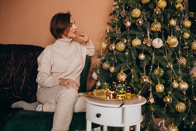 Donna felice che si siede sul sofà dall'albero di Natale