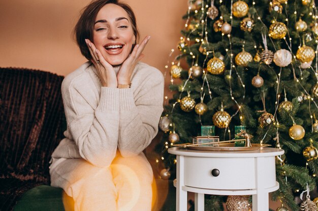 Donna felice che si siede sul sofà dall'albero di Natale