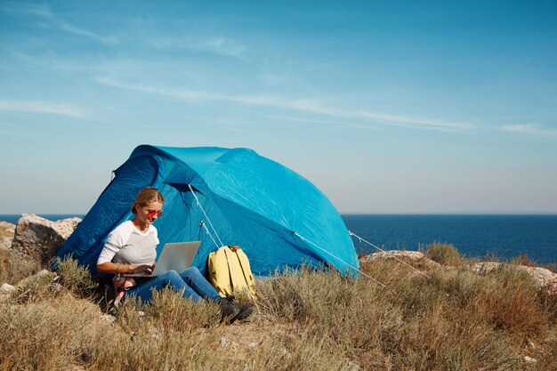 Donna felice che si siede vicino alla tenda con il computer portatile