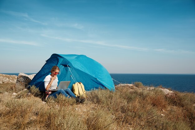 Donna felice che si siede vicino alla tenda con il computer portatile